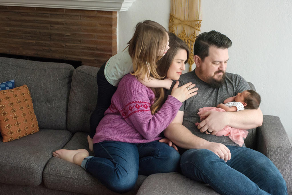 A family hugs around a newborn baby on the couch