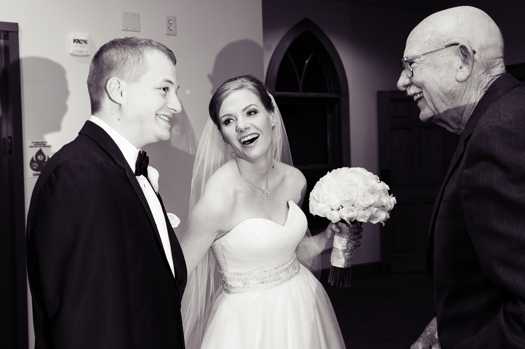 bride laughs at groom as a wedding guests talks to them