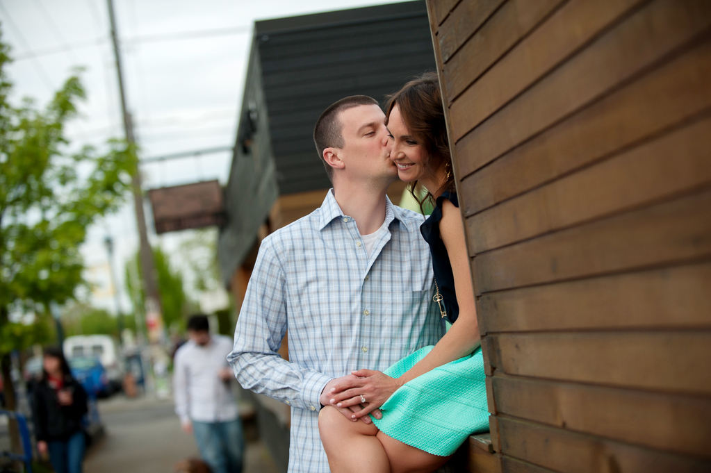 a man kisses his fiances cheek as she sits on the wall at cruz room on alberta street