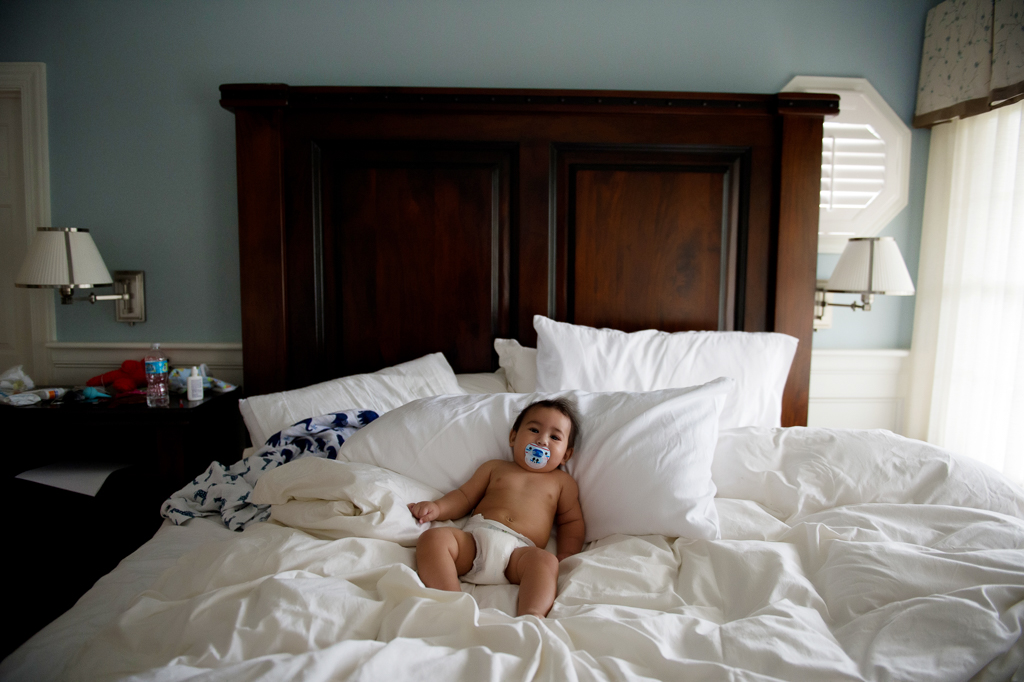 a baby in a diaper lays in a pile of pillows on a large bed