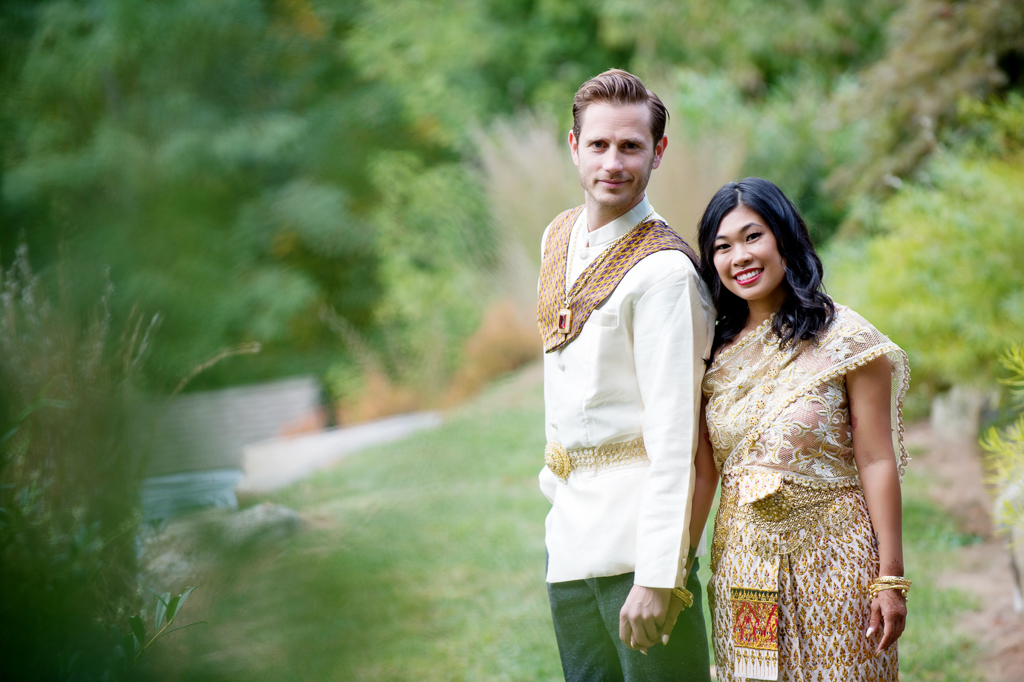 a man and woman in traditional gold cambodian wedding attire smiles at the camera