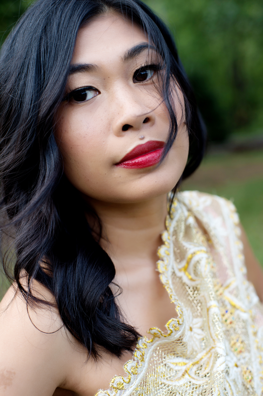 a woman in traditional gold cambodian wedding attire and red lipstick looks intently at the camera