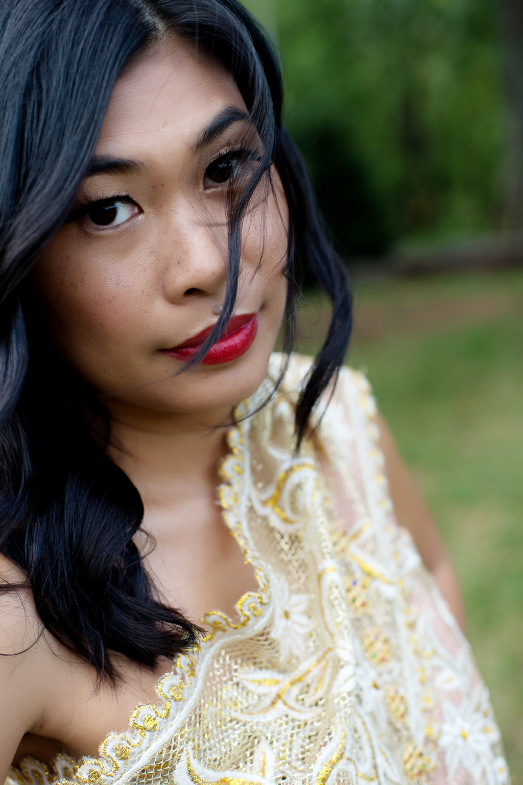 a woman in traditional gold cambodian wedding attire and red lipstick looks intently at the camera
