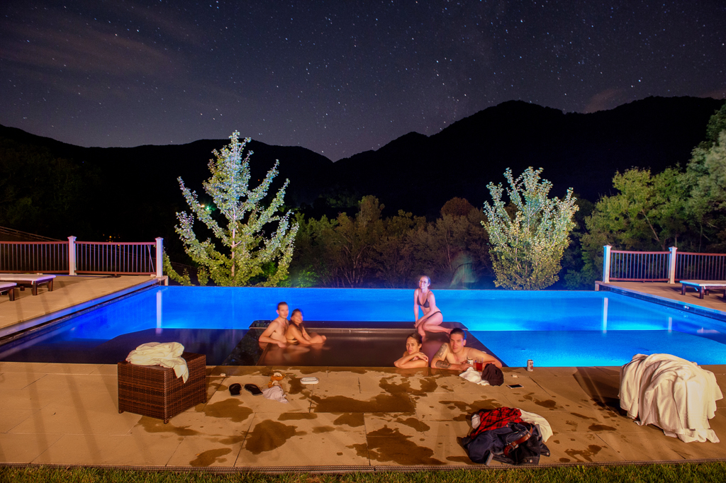 people sit in an infinity pool under the stars at night with the blue ridge mountains in the distance