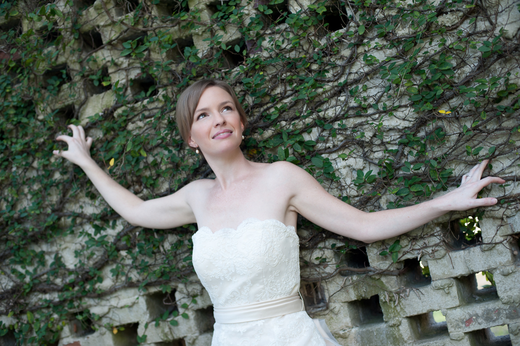 a bride leans against a wall covered in ivy and vines