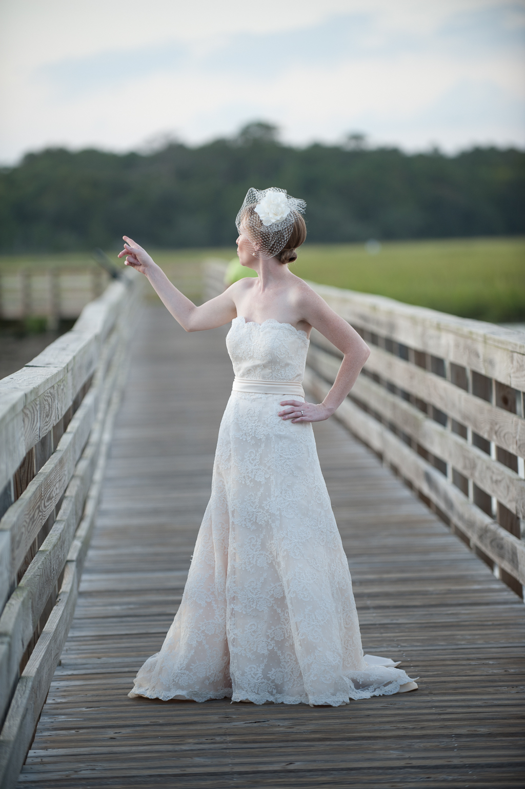 a bride wearing a birdcage veil stands on a boardwalk over murrells inlet