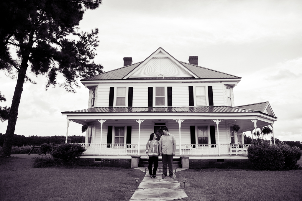 couple stands in front of their old white farmhouse