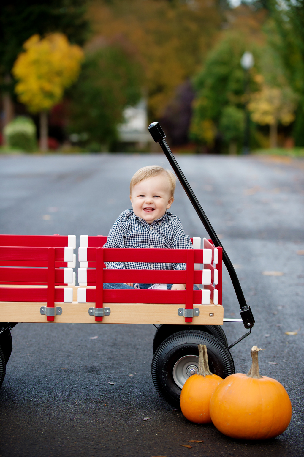 a baby boy sits in a red wagon with pumpkins in front