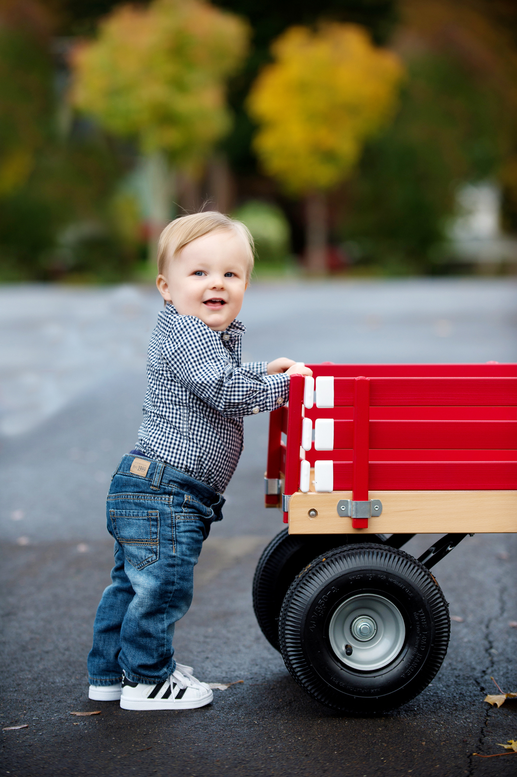 a baby boy stands in the street holding onto a red wagon