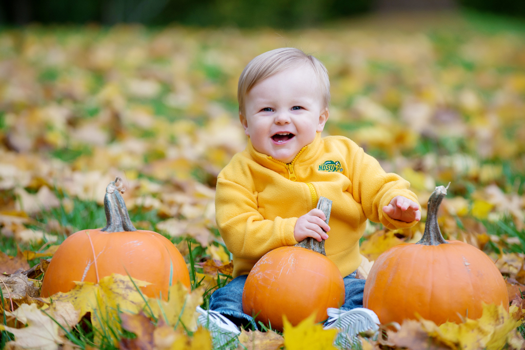 a baby boy sits in a pile of leaves surrounded by pumpkins