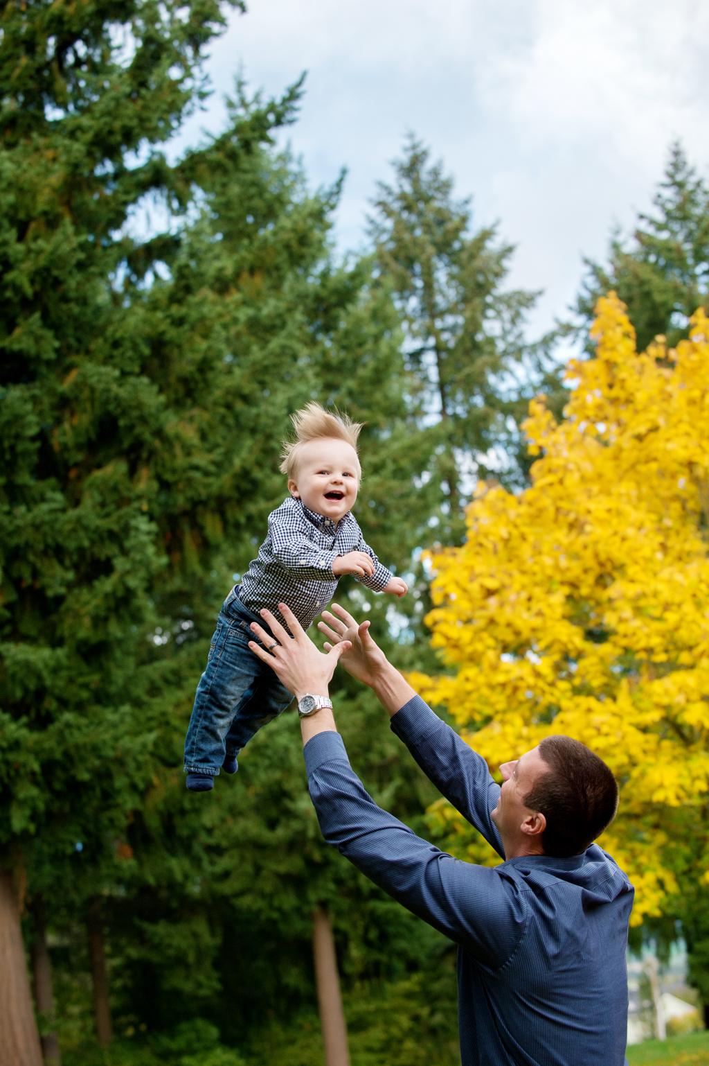 a dad throws up a baby boy in the air with a bright yellow autumn tree in the background