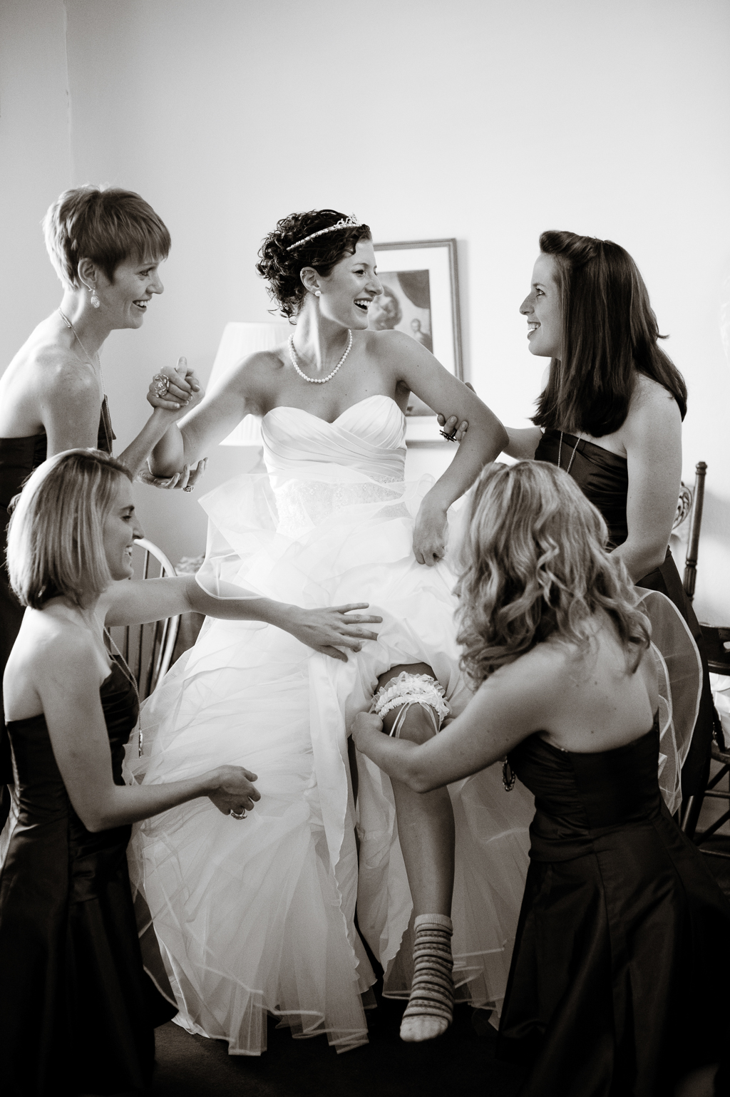 bridesmaids surround a bride and balance her as they put on her garter