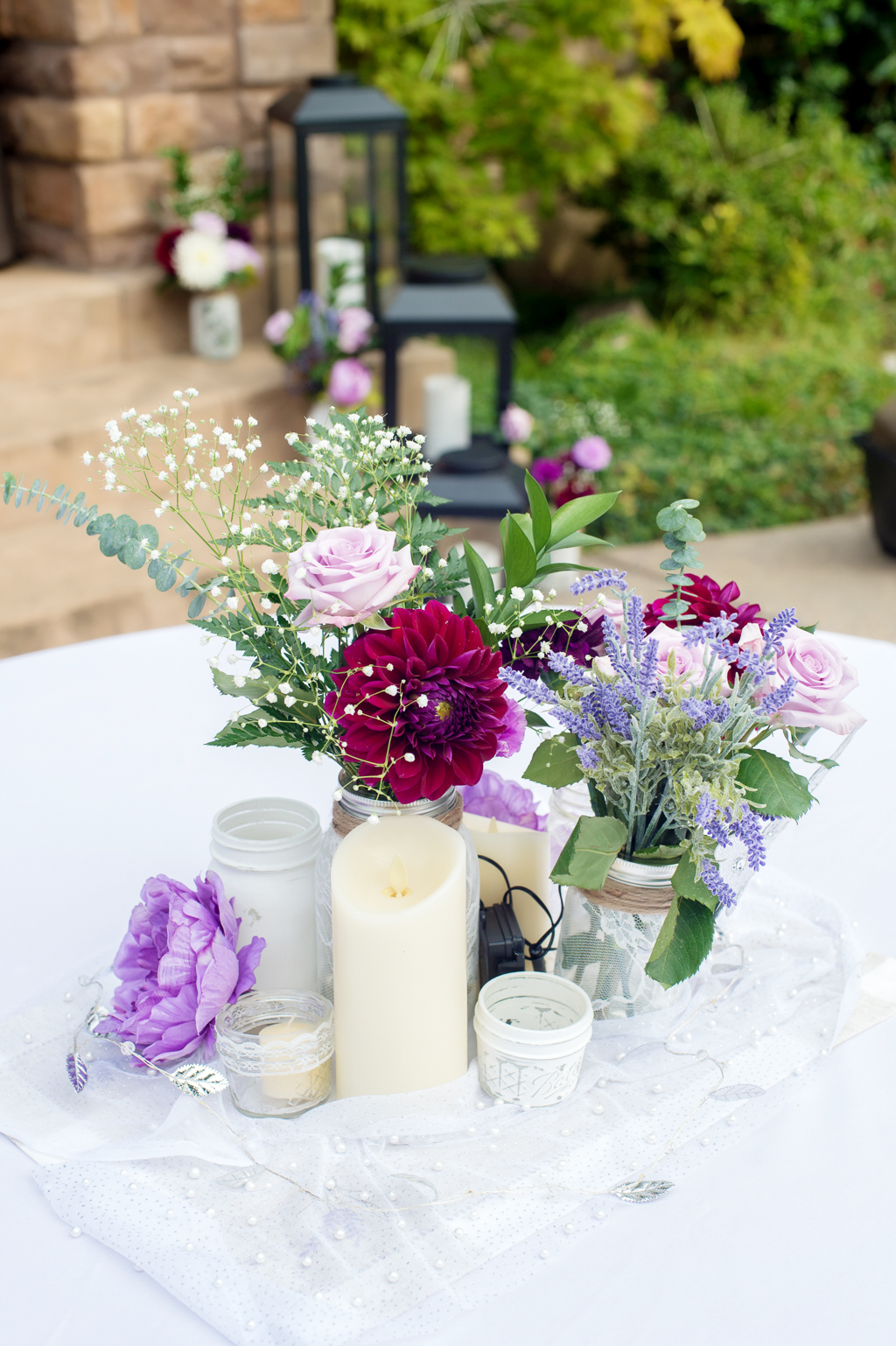 purple and maroon flowers fill mason jars covered in burlap and lace on wedding reception tables