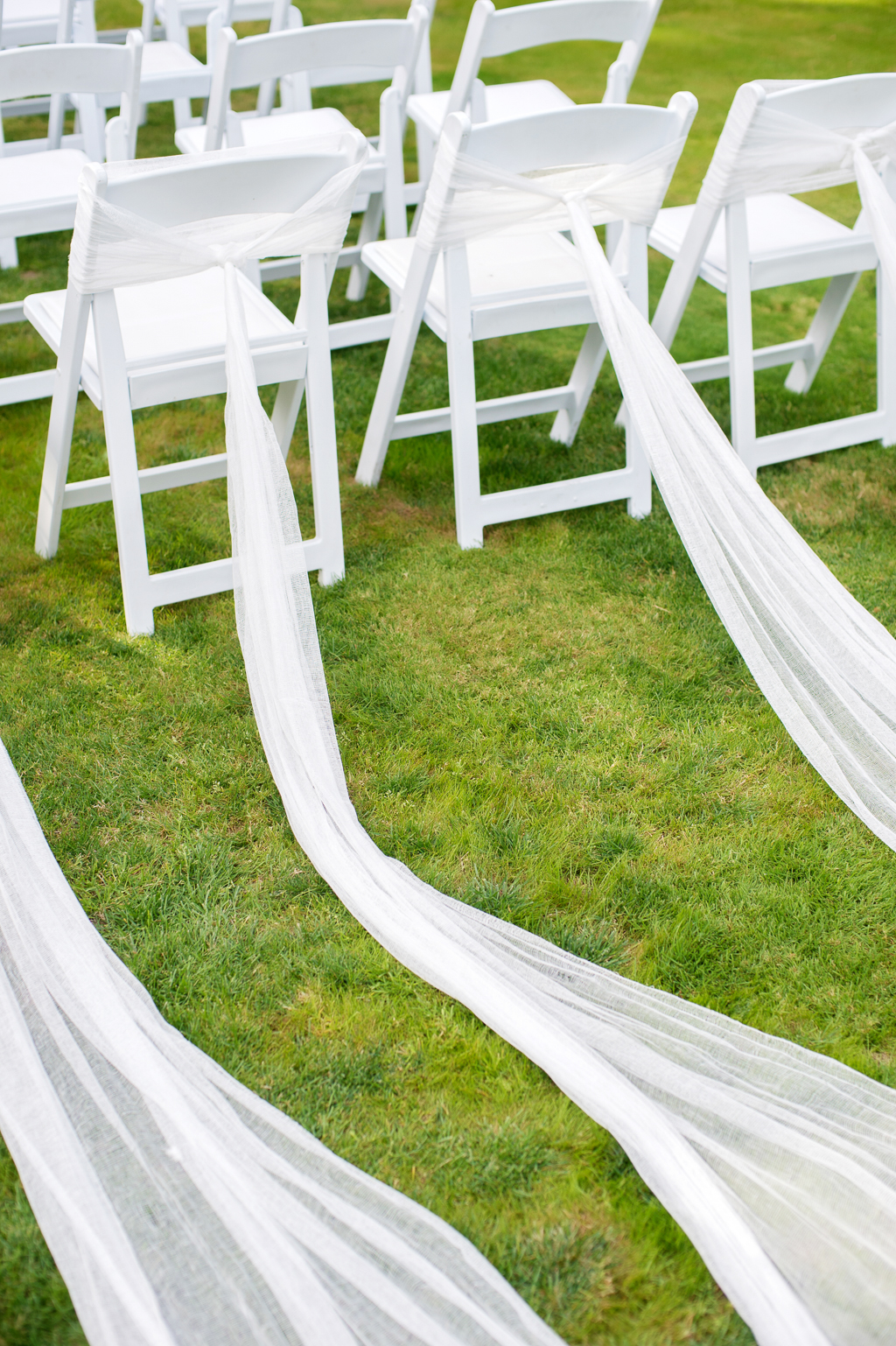 long trails of sheer white fabric spread out behind the last rows of chairs at a wedding ceremony