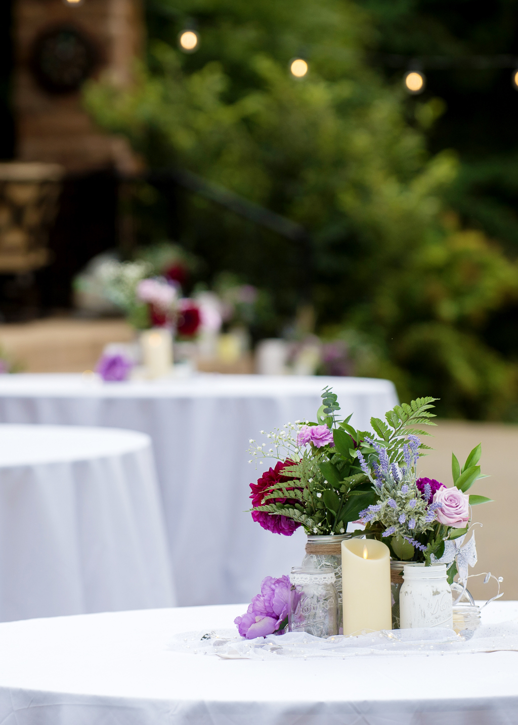 purple and maroon flowers fill mason jars covered in burlap and lace on wedding reception tables