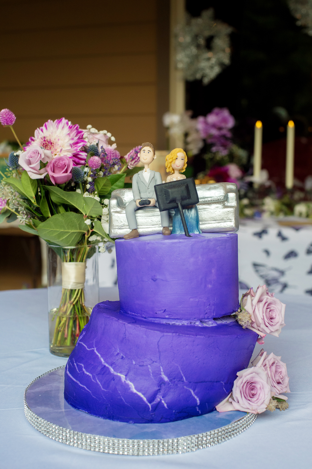 a listing purple wedding cake melted in the heat with a cake topper of a man and woman sitting on a couch playing video games