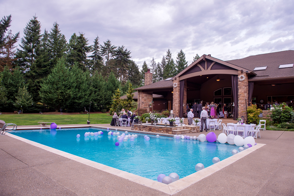 purple gray and white balloons fill a backyard swimming pool for a wedding reception