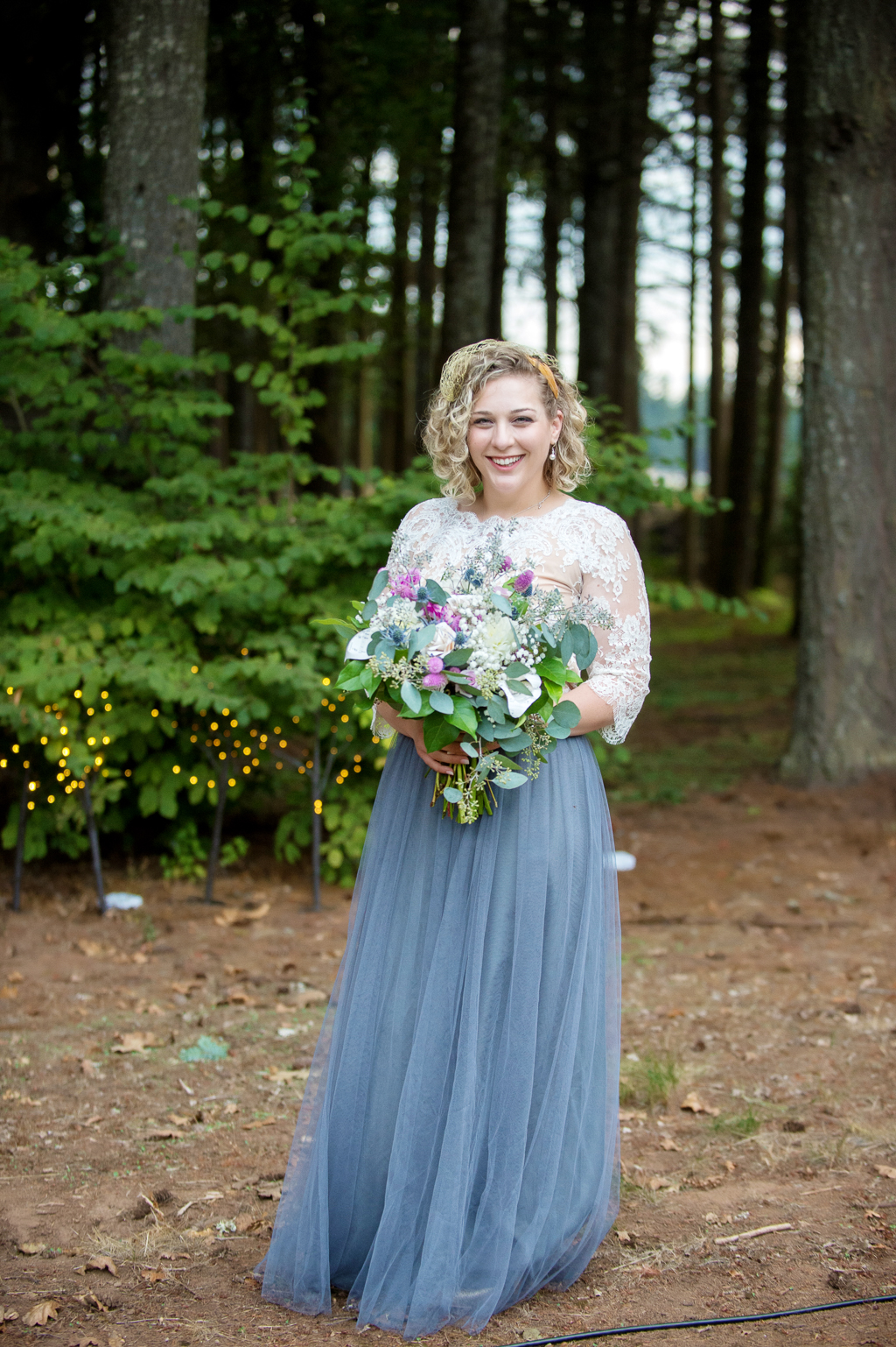 a bride in a lace top with gray flowy skirt holds a pretty purple and ivory wedding bouquet