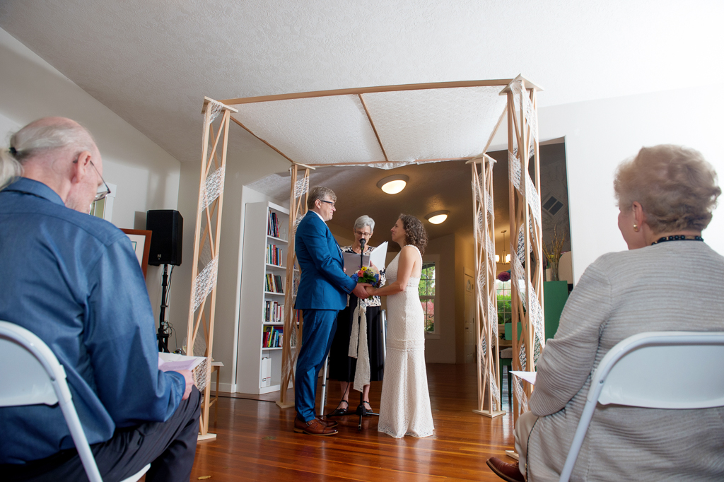 bride and groom stand under chuppah inside house during wedding ceremony