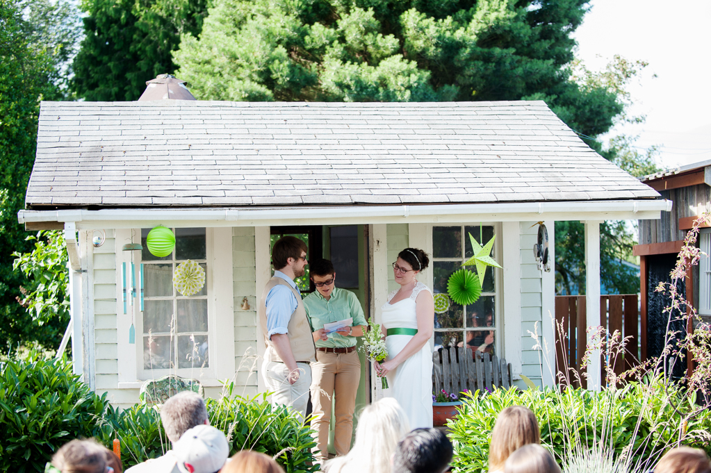 bride and groom get married on the front porch of a garden shed in backyard while wedding guests look on