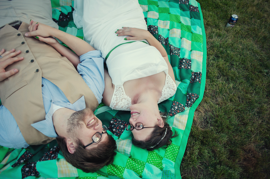 a bride and groom lay in the grass on a colorful bright green quilt