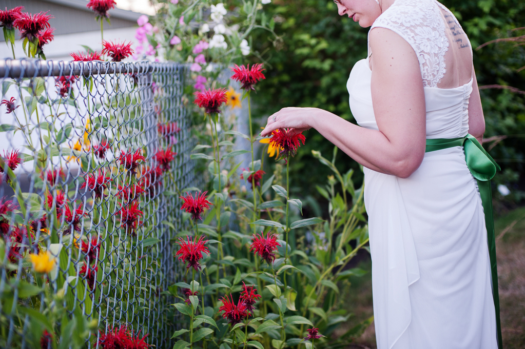 a bride touches a red flower growing next to a fence