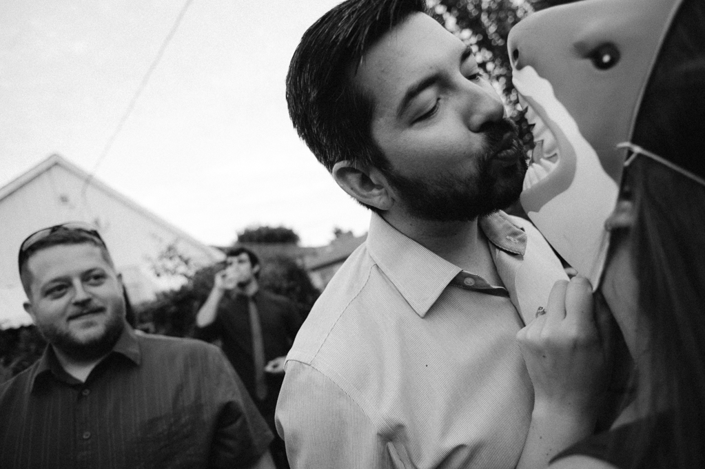 a wedding guest pretends to kiss someone in a shark mask while a man looks on 