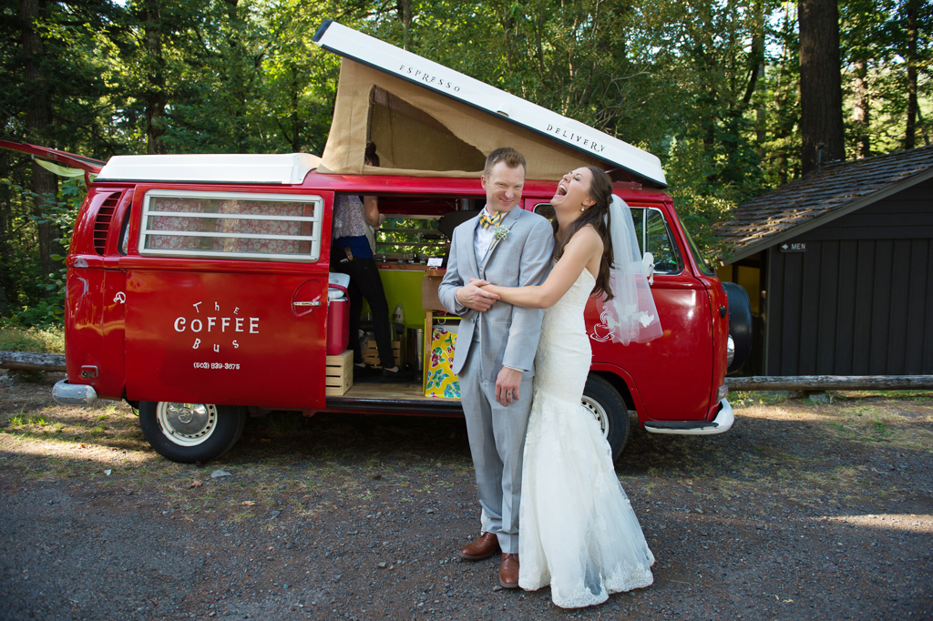 a bride hugs her groom and laughs standing in front of a red vw coffee van