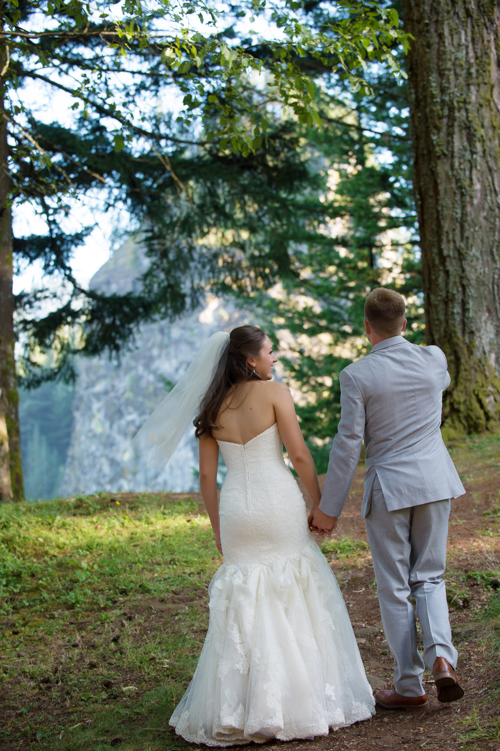 a bride and groom walk toward beacon rock