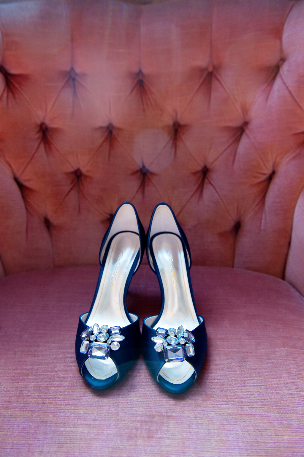 navy blue wedding shoes with diamond rhinestones sit on a pink tufted chair