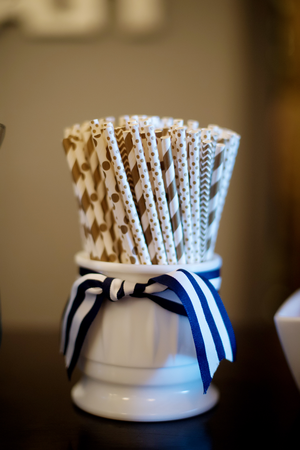 a white jar tied with a navy and blue ribbon with gold and white straws