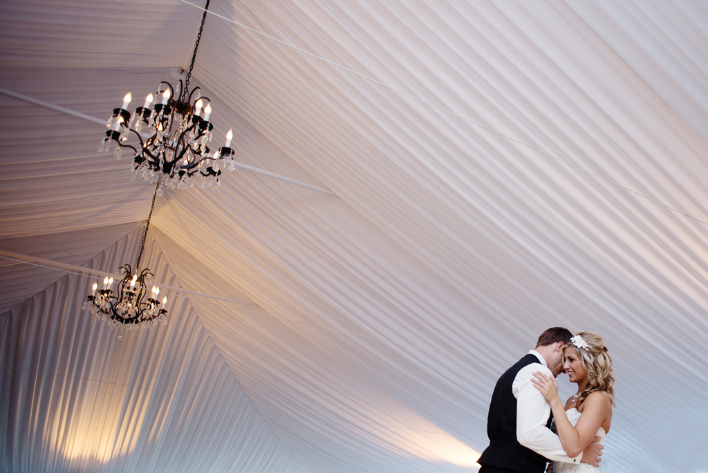 bride and groom first dance under a tent with chandeliers 