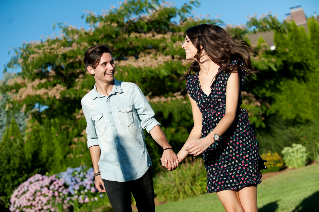 a man and woman run holding hands in front of purple hydrangeas and a mimosa tree