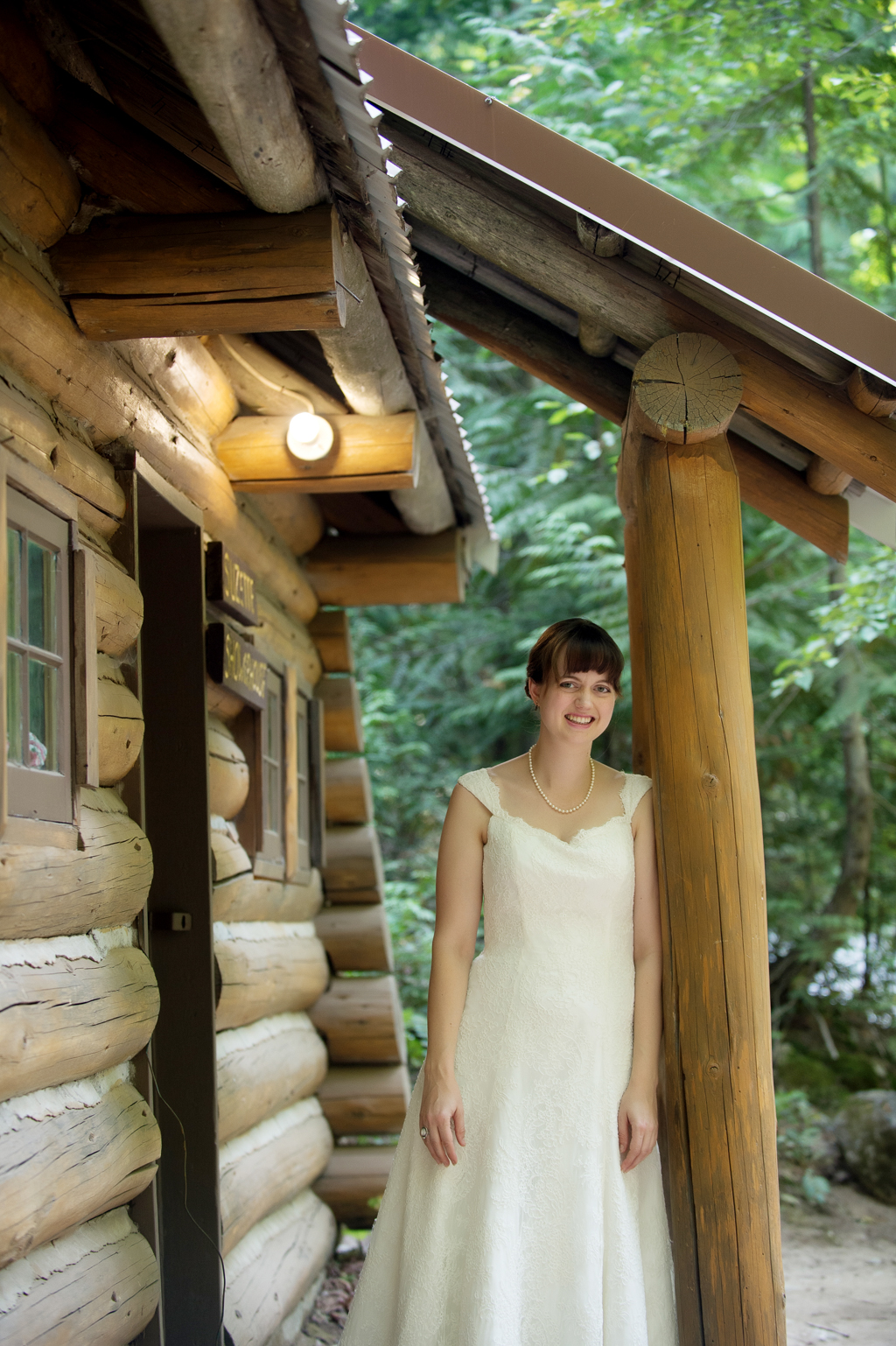 a bride stands on the porch of a summer camp cabin