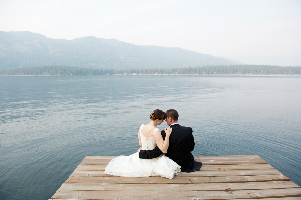 a couple lean together on a dock overlooking a lake with the sky filled with foggy smoke