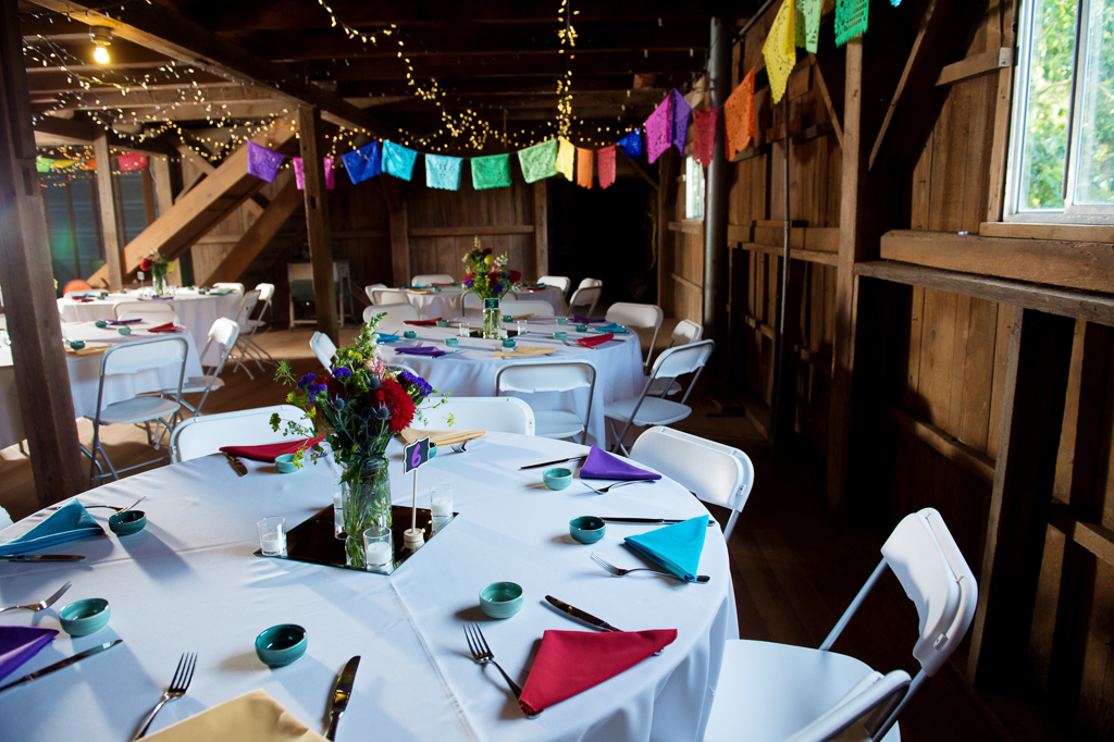 traditional mezcal cups and colorful napkins on the table for wedding reception with Papel picado hanging from rafters