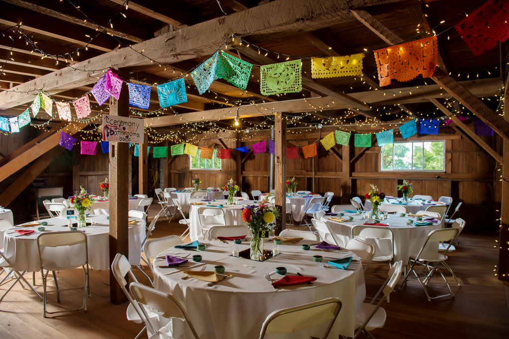 traditional mezcal cups and colorful napkins on the table for wedding reception with Papel picado hanging from rafters