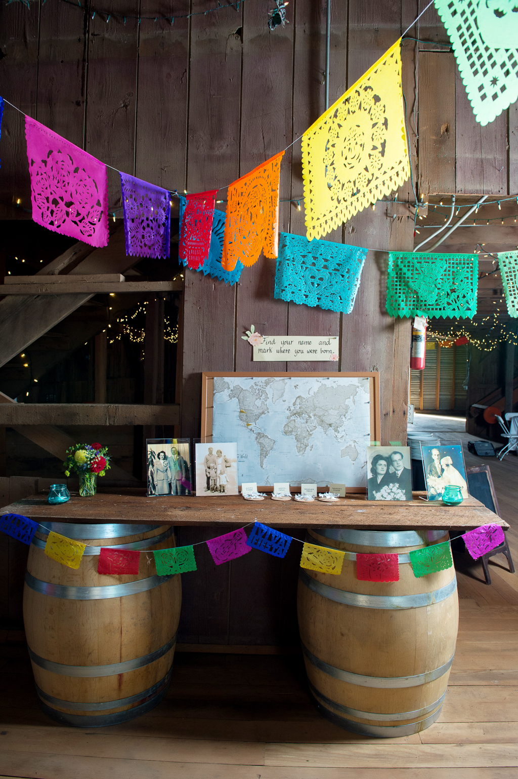 papel picado hang from rafters in a barn for wedding reception decor