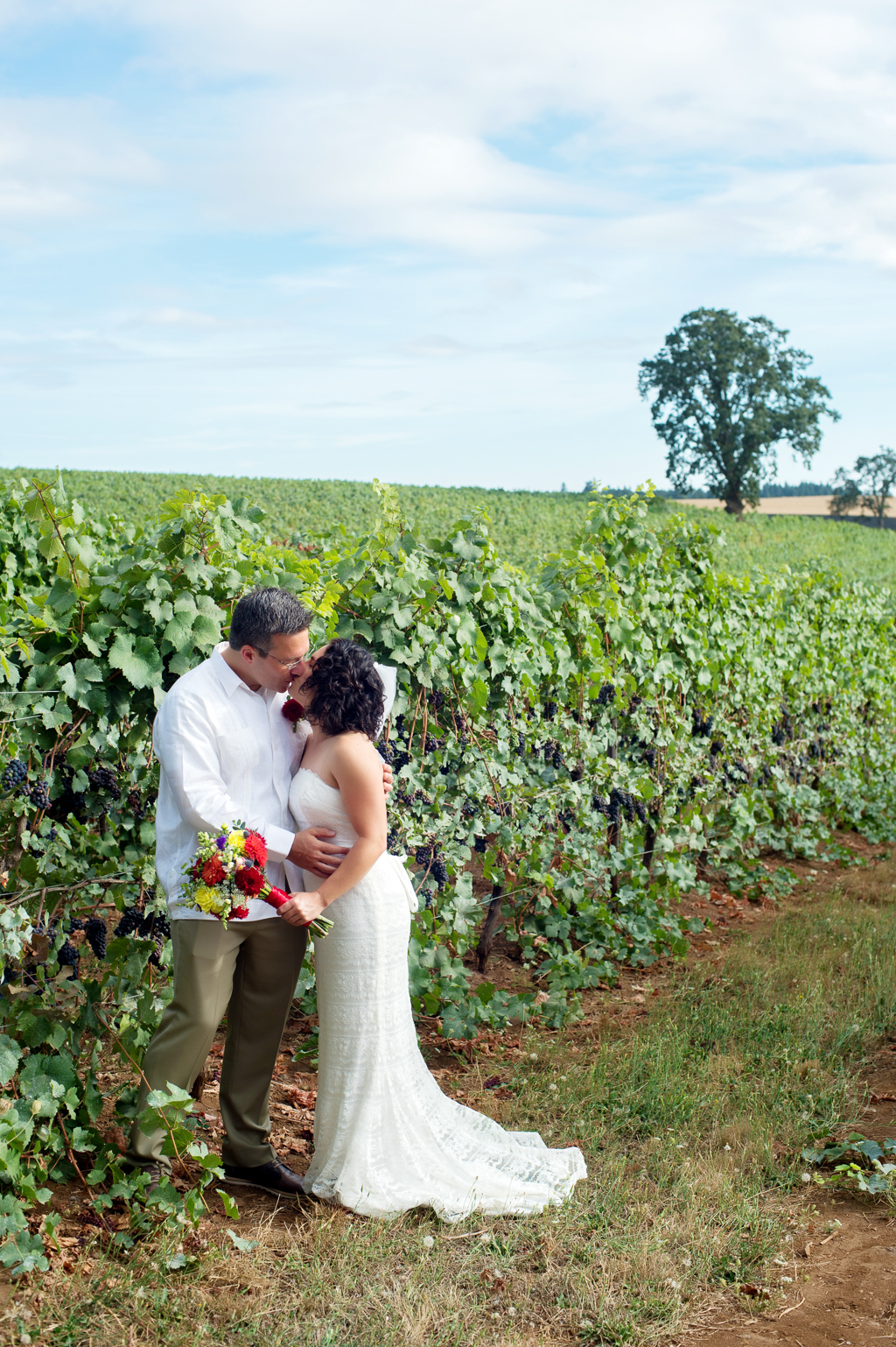 bride with vibrant yellow and red bouquet kisses her groom in a vineyard
