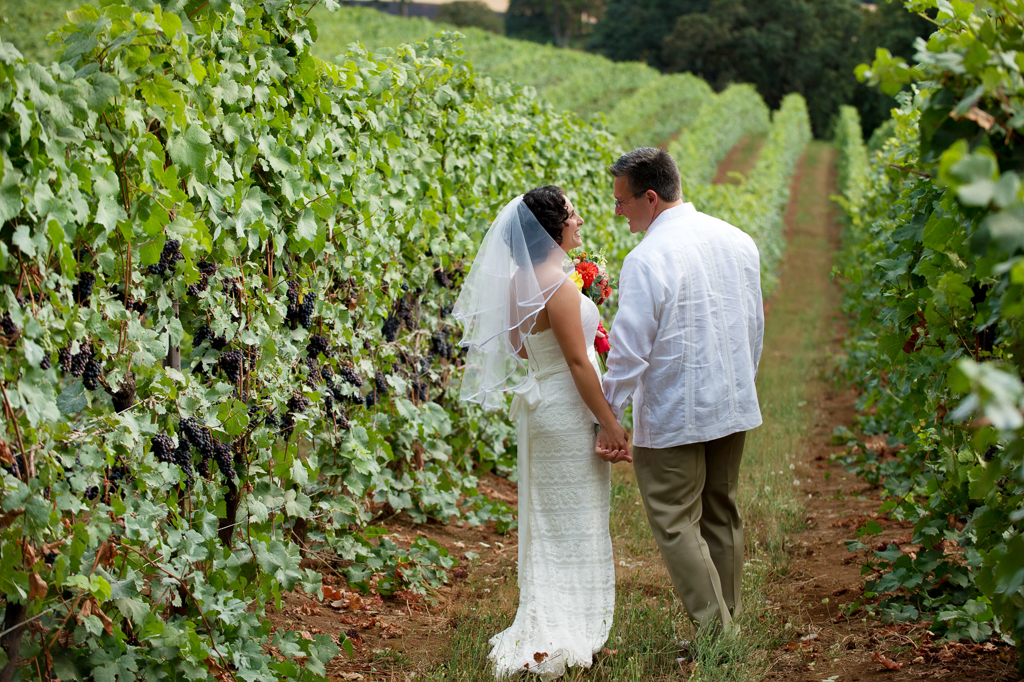 bride with vibrant yellow and red bouquet walks with her groom in a vineyard