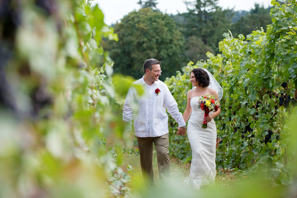 bride with vibrant yellow and red bouquet walks with her groom in a vineyard