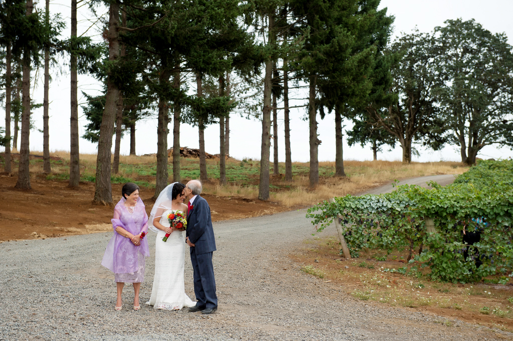 a father kisses the bride's forehead as her mother watches