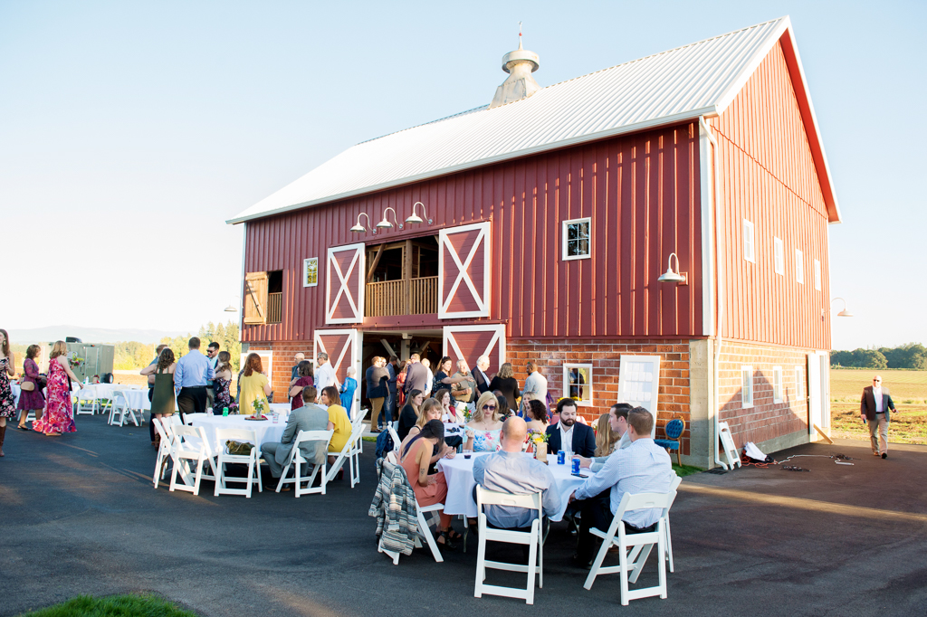 wedding guests gather outside of red barn during reception