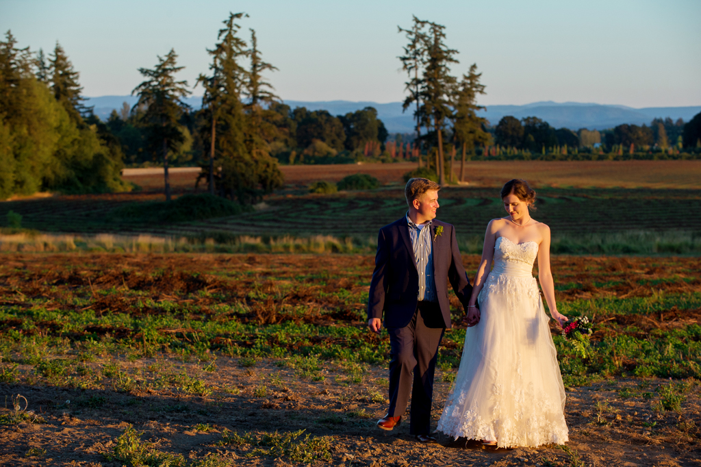 bride and groom walk through country field at sunset
