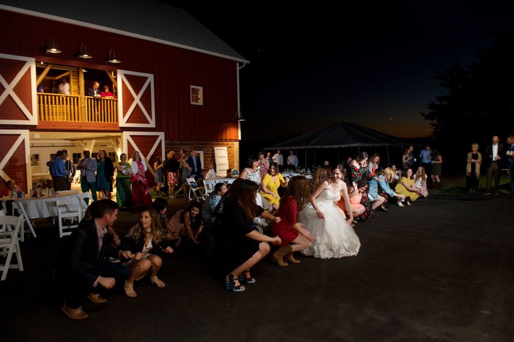 wedding guests dance in front of red barn during wedding reception
