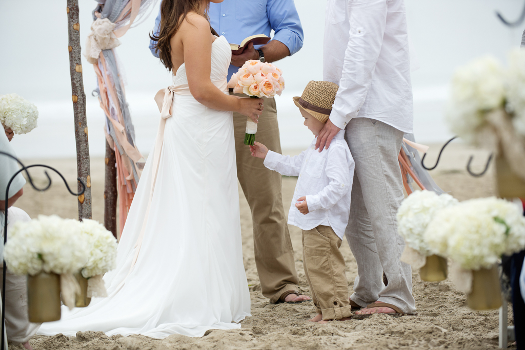 a couple's son plays with the bride's bouquet during the wedding ceremony on the beach