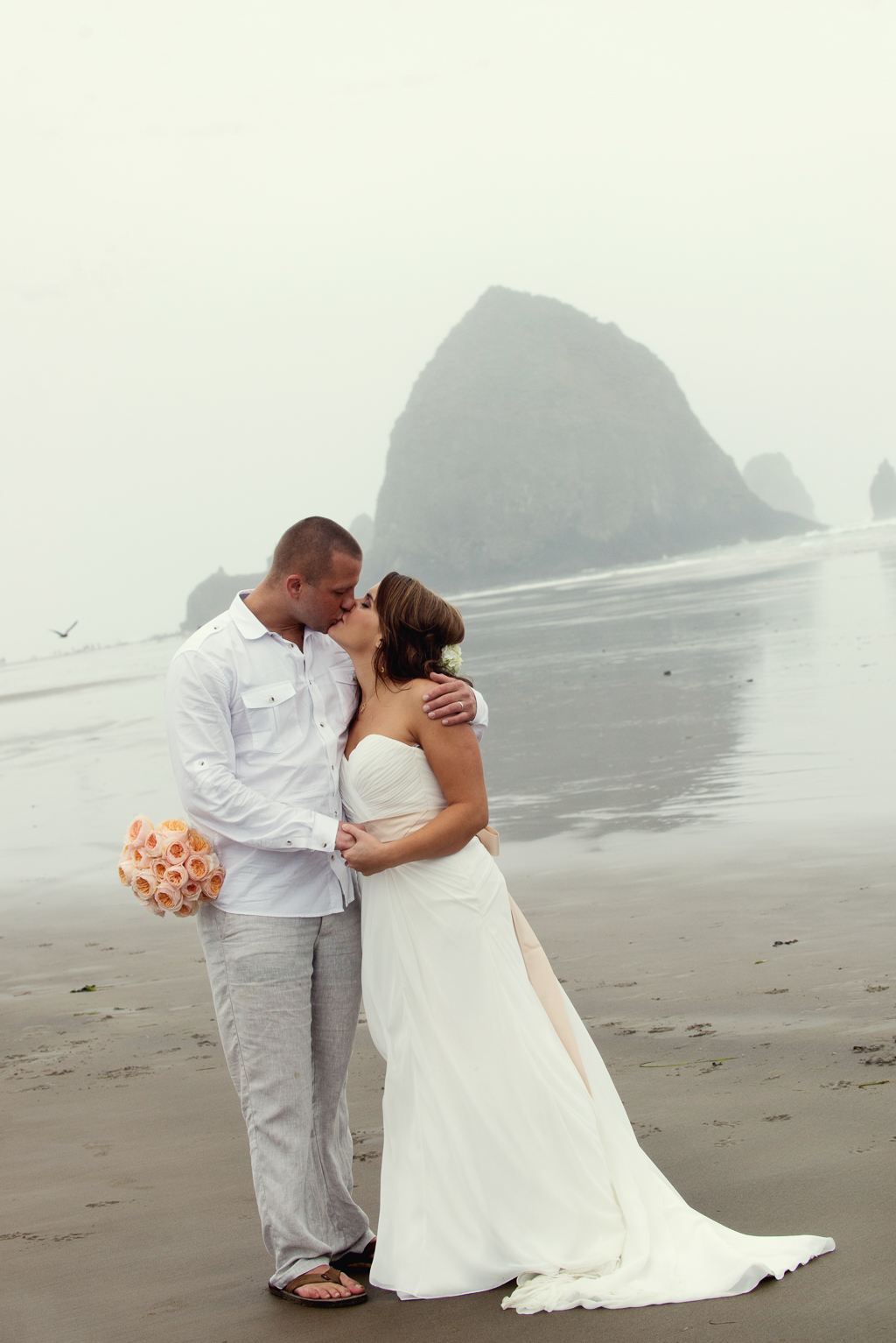 a bride and groom kiss in front of haystack rock on cannon beach
