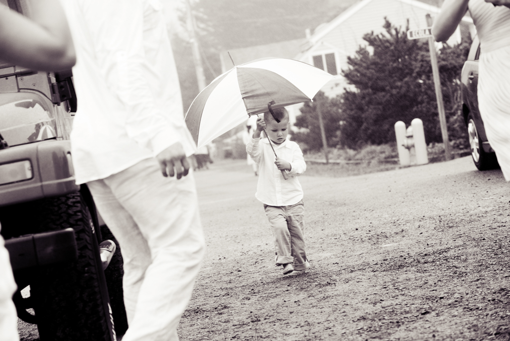 a little boy walks through a large puddle holding an umbrella and dressed for a wedding