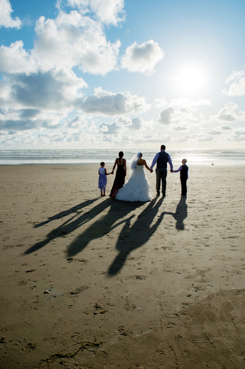 bride and groom with 3 kids walk into sunset on cannon beach