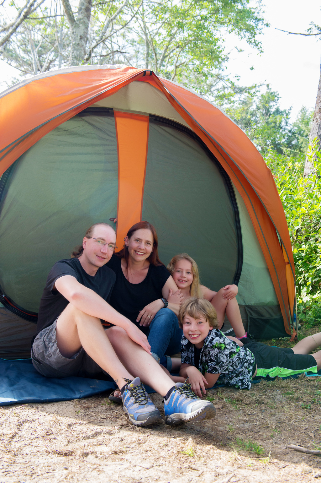family sits in front of orange and green tent